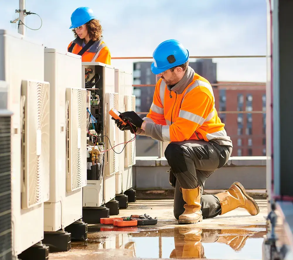 Two field technicians in hard hats servicing rooftop equipment