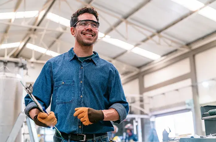A tradesperson smiling on a worksite while holding tools